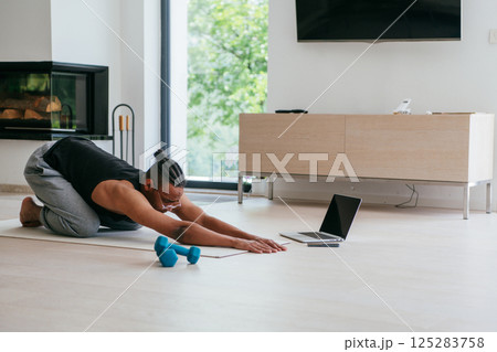 Training At Home. Sporty african american man doing the training while watching an online tutorial on a laptop, exercising in the living room, free space.  125283758