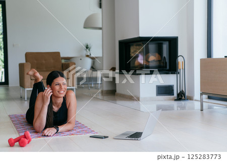 Young woman resting after online training while lying on the living room floor. Young woman resting after online training while lying on the living room floor. 125283773