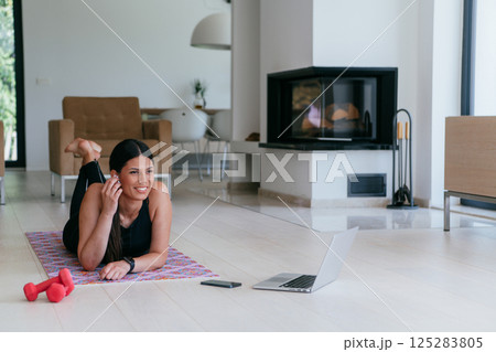 Young woman resting after online training while lying on the living room floor. Young woman resting after online training while lying on the living room floor. 125283805