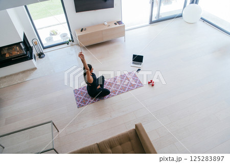 Young Beautiful Female Exercising, Stretching and Practising Yoga with Trainer via Video Call Conference in Bright Sunny House. Healthy Lifestyle, Wellbeing and Mindfulness Concept Young Beautiful Female Exercising, Stretching and Practising Yoga with Trainer via Video Call Conference in Bright Sunny House. Healthy Lifestyle, Wellbeing and Mindfulness Concept 125283897