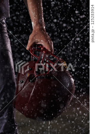 Close up of American Football Athlete Warrior Standing on a Field focus on his Helmet and Ready to Play. Player Preparing to Run, Attack and Score Touchdown. Rainy Night with Dramatic lens flare 125283914