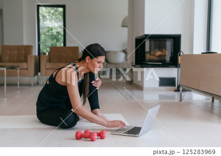 Young Beautiful Female Exercising, Stretching and Practising Yoga with Trainer via Video Call Conference in Bright Sunny House. Healthy Lifestyle, Wellbeing and Mindfulness Concept. Young Beautiful Female Exercising, Stretching and Practising Yoga with Trainer via Video Call Conference in Bright Sunny House. Healthy Lifestyle, Wellbeing and Mindfulness Concept. 125283969