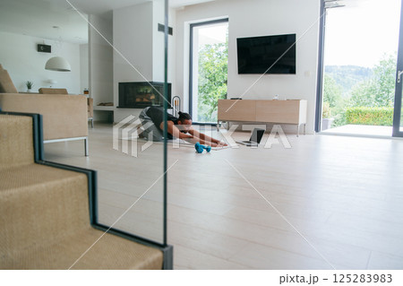 Training At Home. Sporty african american man doing the training while watching an online tutorial on a laptop, exercising in the living room, free space. Training At Home. Sporty african american man doing the training while watching an online tutorial on a laptop, exercising in the living room, free space. 125283983