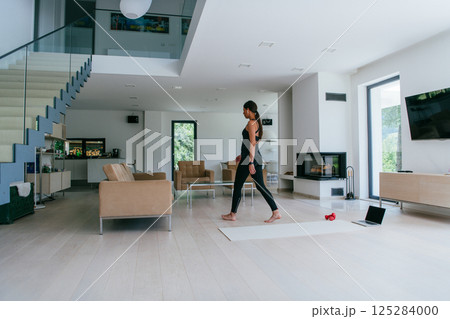 Young Beautiful Female Exercising, Stretching and Practising Yoga with Trainer via Video Call Conference in Bright Sunny House. Healthy Lifestyle, Wellbeing and Mindfulness Concept Young Beautiful Female Exercising, Stretching and Practising Yoga with Trainer via Video Call Conference in Bright Sunny House. Healthy Lifestyle, Wellbeing and Mindfulness Concept 125284000
