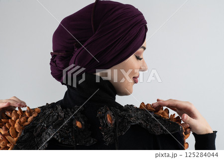 A stylish Muslim woman in a hijab presents her innovative handmade fashion accessory crafted from dried plums in a professional studio. 125284044