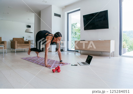 Young Beautiful Female Exercising, Stretching and Practising Yoga with Trainer via Video Call Conference in Bright Sunny House. Healthy Lifestyle, Wellbeing and Mindfulness Concept 125284051