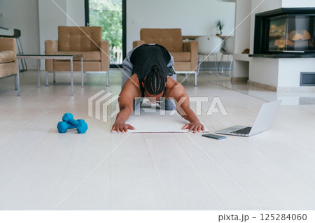 Training At Home. Sporty african american man doing the training while watching an online tutorial on a laptop, exercising in the living room, free space. Training At Home. Sporty african american man doing the training while watching an online tutorial on a laptop, exercising in the living room, free space. 125284060
