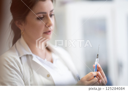 A focused nurse in a white lab coat carefully prepares a syringe for an injection in a professional healthcare environment. A focused nurse in a white lab coat carefully prepares a syringe for an injection in a professional healthcare environment. 125284084