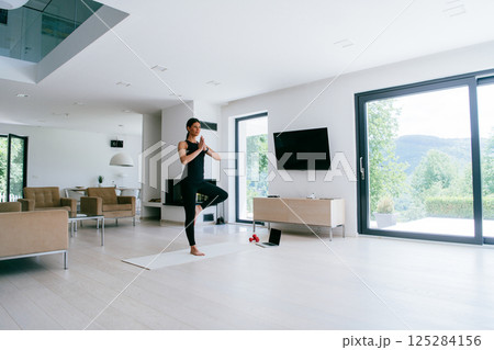 Young Beautiful Female Exercising, Stretching and Practising Yoga with Trainer via Video Call Conference in Bright Sunny House. Healthy Lifestyle, Wellbeing and Mindfulness Concept Young Beautiful Female Exercising, Stretching and Practising Yoga with Trainer via Video Call Conference in Bright Sunny House. Healthy Lifestyle, Wellbeing and Mindfulness Concept 125284156