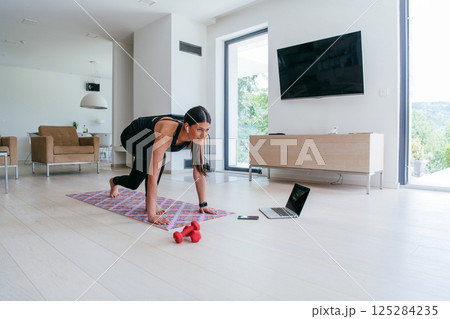 Young Beautiful Female Exercising, Stretching and Practising Yoga with Trainer via Video Call Conference in Bright Sunny House. Healthy Lifestyle, Wellbeing and Mindfulness Concept 125284235