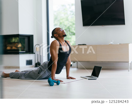 Training At Home. Sporty man doing the training while watching an online tutorial on a laptop, exercising in the living room, free space. Training At Home. Sporty man doing the training while watching an online tutorial on a laptop, exercising in the living room, free space. 125284243