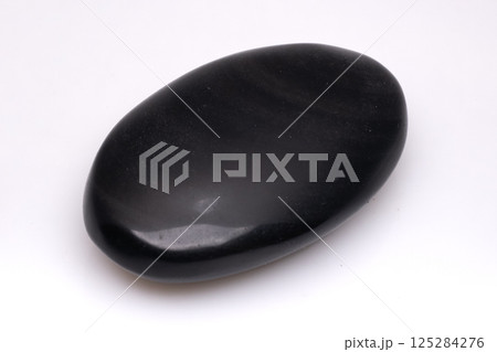 Polished black river stone isolated on a white background with subtle light reflections creating a smooth, glossy appearance and natural texture 125284276