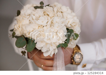 Elegant Wedding Bouquet Held by Groom's Hand with White Hydrangeas, Eucalyptus and Gold Watch Detail, Celebrating Love and Commitment Elegant Wedding Bouquet Held by Groom's Hand with White Hydrangeas, Eucalyptus and Gold Watch Detail, Celebrating Love and Commitment 125284314