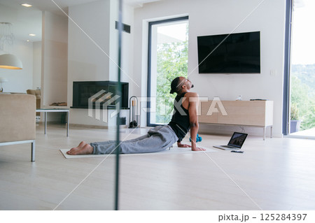 Training At Home. Sporty african american man doing the training while watching an online tutorial on a laptop, exercising in the living room, free space. Training At Home. Sporty african american man doing the training while watching an online tutorial on a laptop, exercising in the living room, free space. 125284397