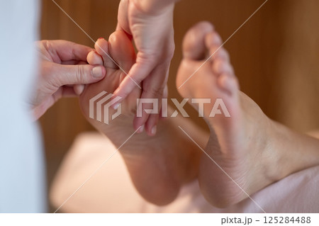 Foot Massage Therapy in a Relaxing Spa Setting. A professional massage therapist in a white uniform provides a soothing foot massage to a client in a calm and serene spa environment 125284488