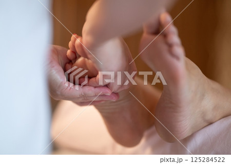 Foot Massage Therapy in a Relaxing Spa Setting. A professional massage therapist in a white uniform provides a soothing foot massage to a client in a calm and serene spa environment Foot Massage Therapy in a Relaxing Spa Setting. A professional massage therapist in a white uniform provides a soothing foot massage to a client in a calm and serene spa environment 125284522