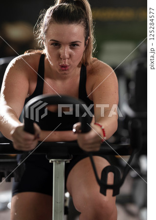 A focused fitness woman performing a conditioning workout in the gym, pushing her limits with strength, determination, and intense dedication. A focused fitness woman performing a conditioning workout in the gym, pushing her limits with strength, determination, and intense dedication. 125284577