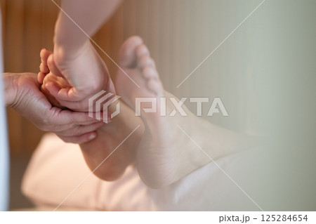 Foot Massage Therapy in a Relaxing Spa Setting. A professional massage therapist in a white uniform provides a soothing foot massage to a client in a calm and serene spa environment Foot Massage Therapy in a Relaxing Spa Setting. A professional massage therapist in a white uniform provides a soothing foot massage to a client in a calm and serene spa environment 125284654