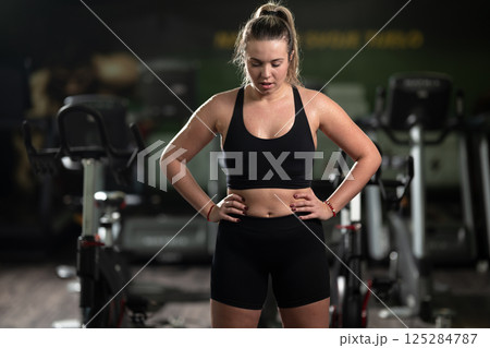 A fit woman strikes a confident pose in the gym after an intense workout, showcasing her strength, dedication, and progress. 125284787