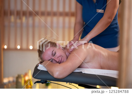 Relaxing Back Massage in a Spa Setting. A professional massage therapist in a blue uniform provides a relaxing back massage to a client lying on a massage table. 125284788