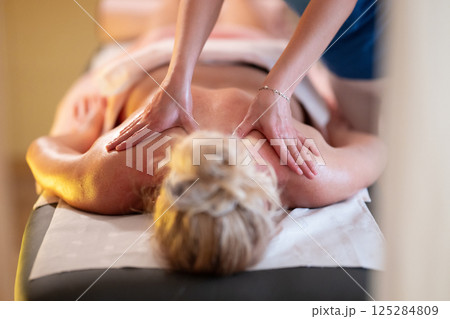 Relaxing Back Massage in a Spa Setting. A professional massage therapist in a blue uniform provides a relaxing back massage to a client lying on a massage table. Relaxing Back Massage in a Spa Setting. A professional massage therapist in a blue uniform provides a relaxing back massage to a client lying on a massage table. 125284809