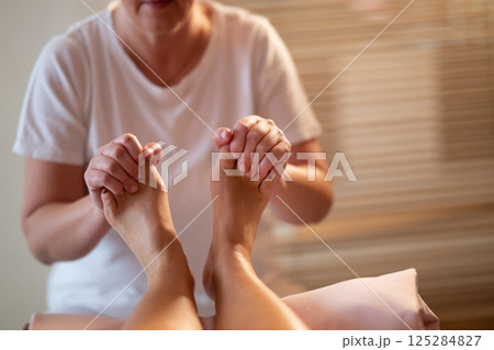 Foot Massage Therapy in a Relaxing Spa Setting. A professional massage therapist in a white uniform provides a soothing foot massage to a client in a calm and serene spa environment Foot Massage Therapy in a Relaxing Spa Setting. A professional massage therapist in a white uniform provides a soothing foot massage to a client in a calm and serene spa environment 125284827