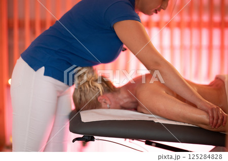 Relaxing Back Massage in a Spa Setting. A professional massage therapist in a blue uniform provides a relaxing back massage to a client lying on a massage table. 125284828
