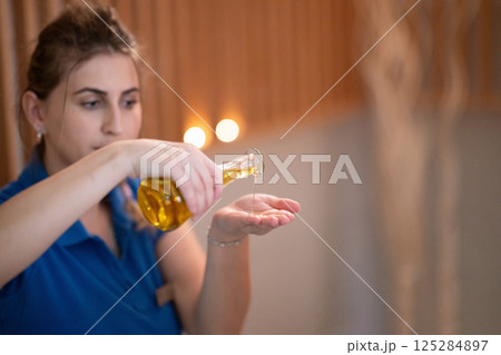 A professional massage therapist pours aromatic oil into their hands, preparing for a relaxing and rejuvenating massage session in a serene spa setting. 125284897