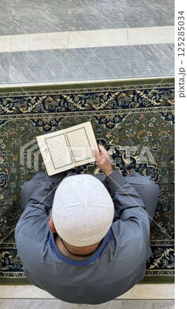 Mecca, Saudi Arabia - May 2, 2024: Young man, Hajj and Umrah pilgrim sitting and reading Quran in Masjidil Haram, Great Mosque in Makkah, Saudi Arabia. Hajj 2024. Mecca, Saudi Arabia - May 2, 2024: Young man, Hajj and Umrah pilgrim sitting and reading Quran in Masjidil Haram, Great Mosque in Makkah, Saudi Arabia. Hajj 2024. 125285034