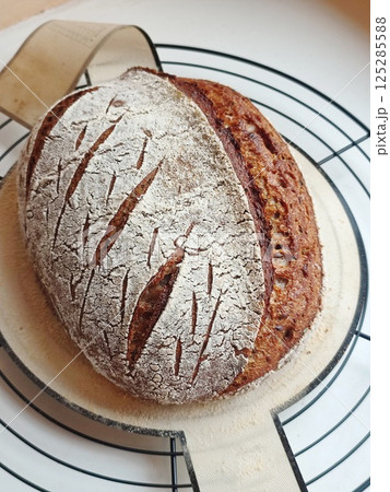 freshly baked artisanal whole wheat sourdough bread with rustic crust cooling on a round metal rack and silicone pad 125285588