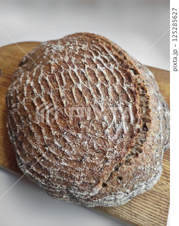 freshly baked artisanal whole wheat sourdough bread with rustic crust cooling on a wooden surface siide view 125285627