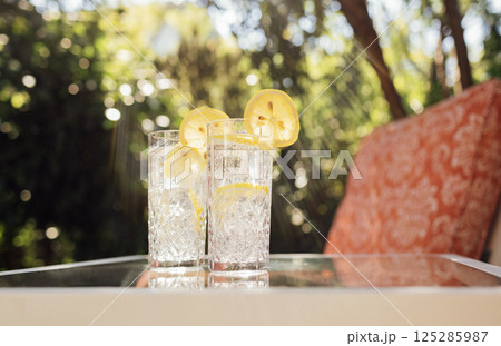 Crystal glasses with delicious cool lemonade on a glass table in the backyard of the house 125285987