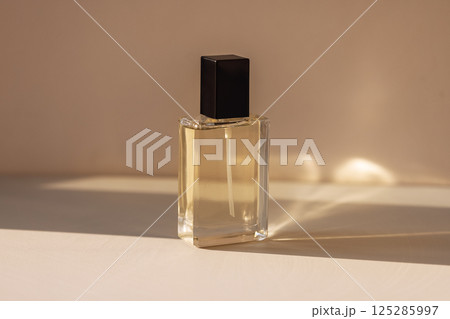 Close-up of a transparent glass elegant perfume bottle with a black lid. A mock-up of a vial of fragrant water on a light background. Cosmetic products. 125285997