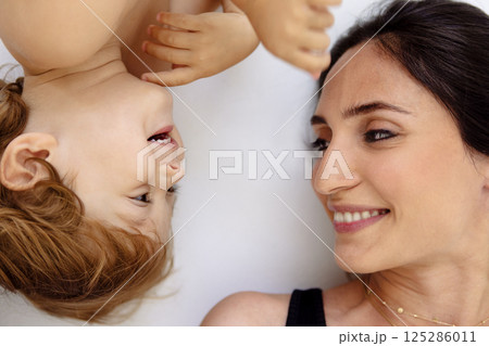 A close-up portrait in profile of a laughing mother and a cute child. A smiling woman and her little son are lying on a white floor. A close-up portrait in profile of a laughing mother and a cute child. A smiling woman and her little son are lying on a white floor. 125286011