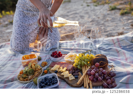 Close-up of a woman hand holding a bottle of wine and pouring white wine into glasses outdoors Close-up of a woman hand holding a bottle of wine and pouring white wine into glasses outdoors 125286038