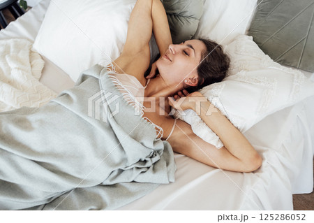 An attractive happy young woman is lying in bed with her eyes closed An attractive happy young woman is lying in bed with her eyes closed 125286052