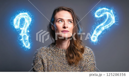 A woman stands in a studio with a neutral background. She appears thoughtful, with glowing question marks appearing on either side, conveying curiosity and introspection. 125286356