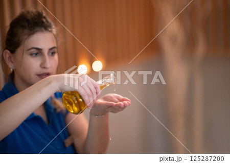 A professional massage therapist pours aromatic oil into their hands, preparing for a relaxing and rejuvenating massage session in a serene spa setting. 125287200