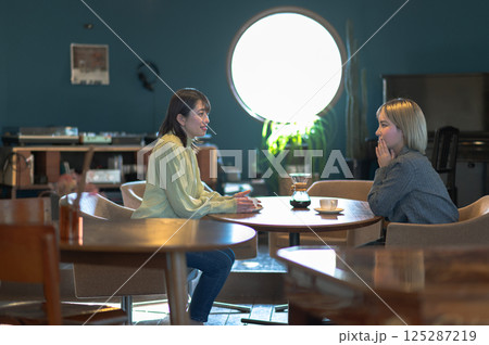 丸い窓の喫茶店でコーヒーを飲む二人の女性 125287219