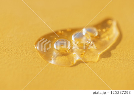 Extremely close-up view of a transparent gel with bubbles and colloidal gold. Cosmetic products. A drop of moisturizing serum or essence on a bright yellow background. Extremely close-up view of a transparent gel with bubbles and colloidal gold. Cosmetic products. A drop of moisturizing serum or essence on a bright yellow background. 125287298