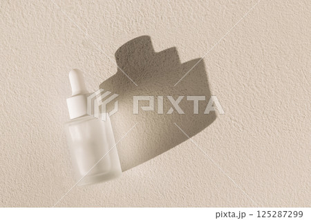 A mock-up of a bottle of moisturizing serum with a pipette on a textured white background. Frosted glass flask with an anti-aging essence dropper. A mock-up of a bottle of moisturizing serum with a pipette on a textured white background. Frosted glass flask with an anti-aging essence dropper. 125287299