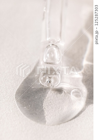 Close-up of a glass pipette with a drop of moisturizing serum with bubbles. Cosmetic products. Vitamin essence with a dropper on a light background. Minimalism. Close-up of a glass pipette with a drop of moisturizing serum with bubbles. Cosmetic products. Vitamin essence with a dropper on a light background. Minimalism. 125287303