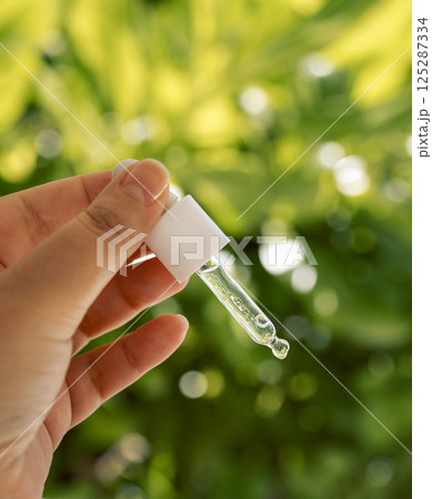 Close-up of a female hand with a dropper and moisturizing facial serum. A young woman holds a cosmetic product. Transparent vitamin essence for skin. 125287334
