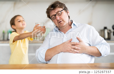 My father heart ached. Little daughter gives her father glass of water My father heart ached. Little daughter gives her father glass of water 125287337