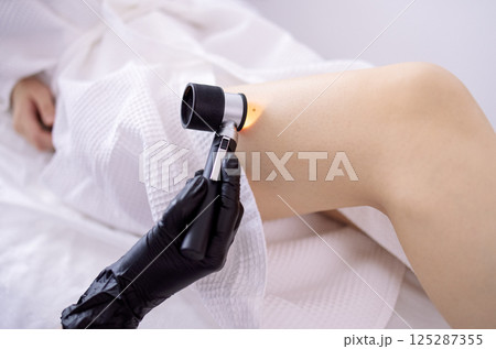 Doctor dermatologist examines skin of client face of beauty salon with a dermatological lens Doctor dermatologist examines skin of client face of beauty salon with a dermatological lens 125287355