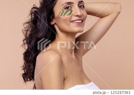 Studio portrait of a young woman with leaves under her eye on a beige 125287361