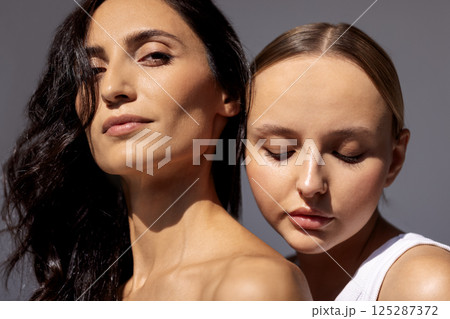 Beauty portrait of two attractive young women with clean healthy skin and hair. Charming models with natural makeup on a gray isolated background. Beauty portrait of two attractive young women with clean healthy skin and hair. Charming models with natural makeup on a gray isolated background. 125287372