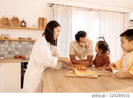 A happy Asian family is eating pizza in the kitchen at home 125289132