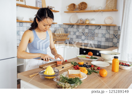 Young attractive Asian woman prepares delicious sandwich with fish and avocado Young attractive Asian woman prepares delicious sandwich with fish and avocado 125289149