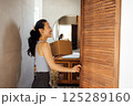 Beautiful young Asian woman takes cardboard box out of closet. Smiling cute female Korean in casual clothes with package in hallway of house. 125289160